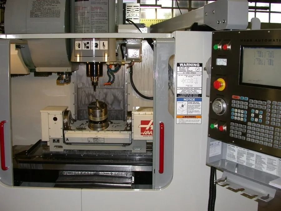 Machine de fraisage CNC dans un atelier, avec panneau de commande et pièce métallique montée à l'intérieur.