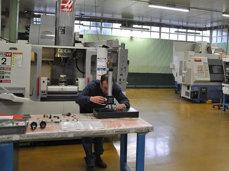 Une personne penchée sur une table de travail dans un atelier d'usinage, avec de gros équipements industriels.
