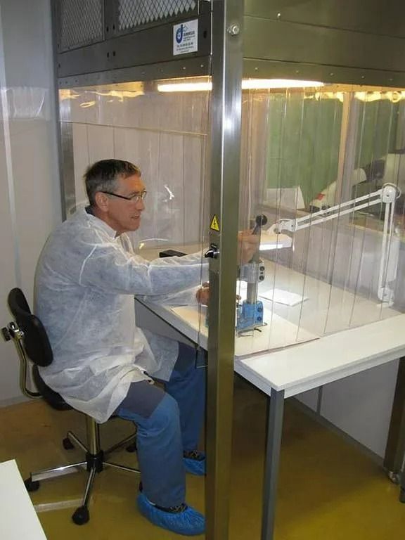 Un homme est assis à un bureau à l'intérieur d'une barrière en plastique transparent, travaillant dans un laboratoire.