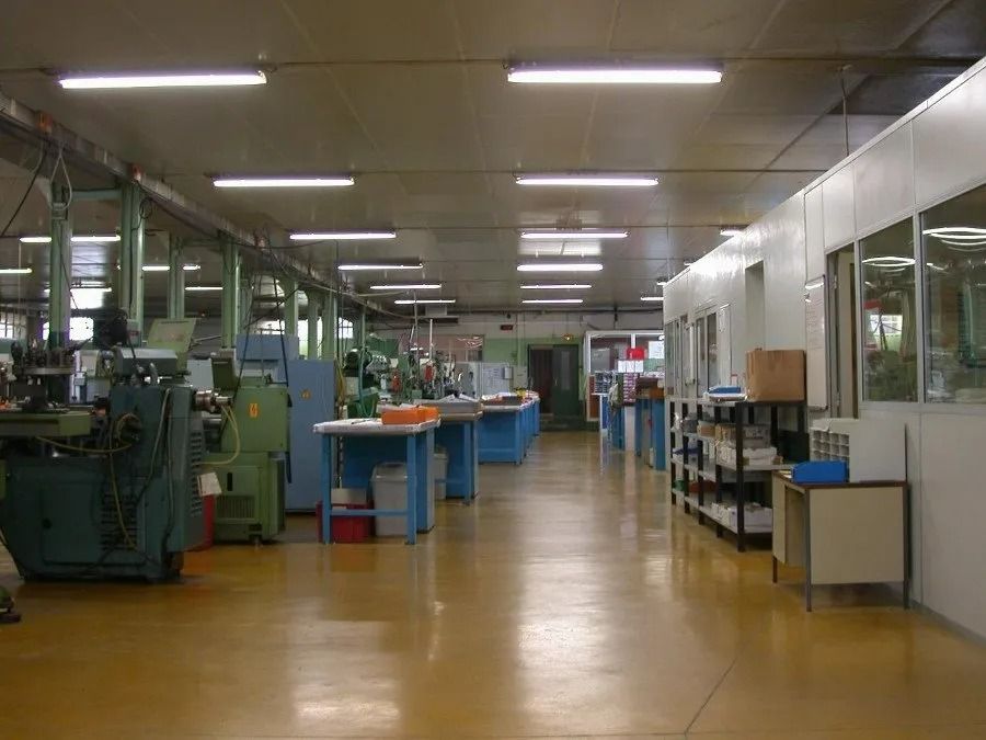 Atelier industriel vide avec machines, tables et éclairage fluorescent au plafond le long d'une longue allée.