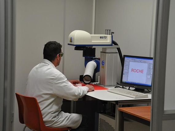 Un scientifique en blouse blanche manipule un poste de travail robotisé équipé d'un écran et d'un ordinateur.