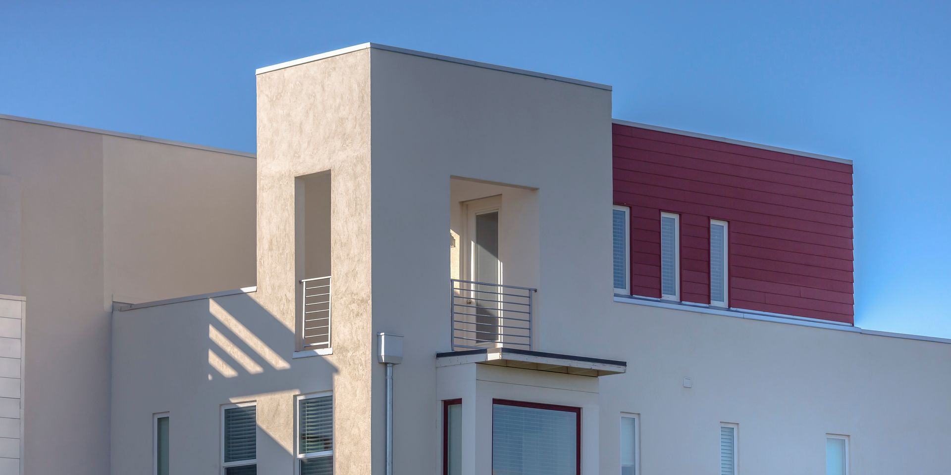 Bâtiment moderne blanc avec des touches de rouge, un balcon et un ciel bleu azur.