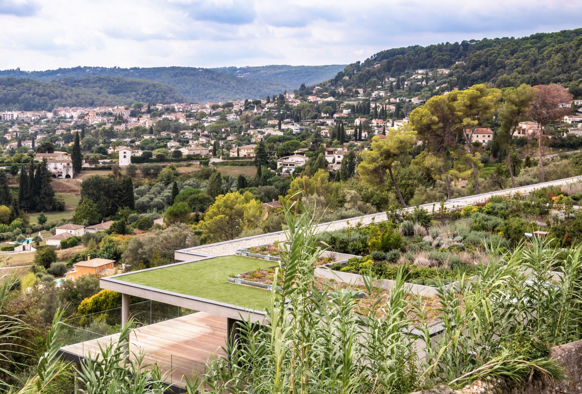 Vue panoramique d'une ville nichée dans une vallée, avec des maisons et une végétation luxuriante sous un ciel nuageux.