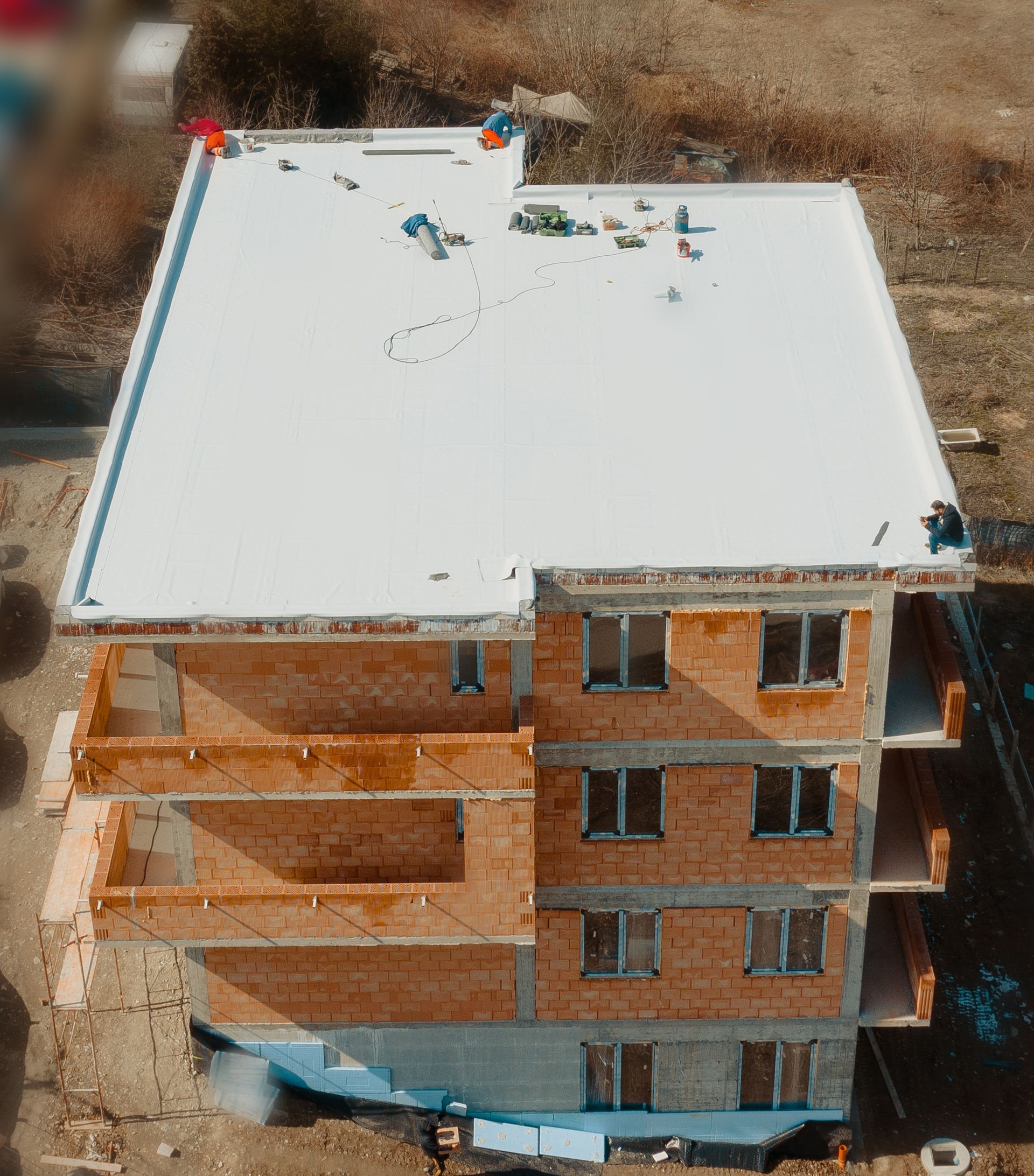 Construction d'un immeuble à plusieurs étages, montrant des murs en briques, des fenêtres, des balcons et des ouvriers sur le toit plat blanc.