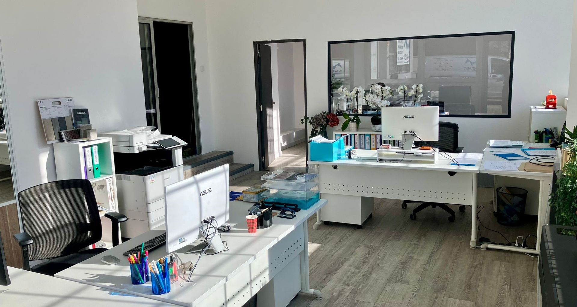 Bureau lumineux avec bureaux, ordinateurs, imprimante et fenêtre.
