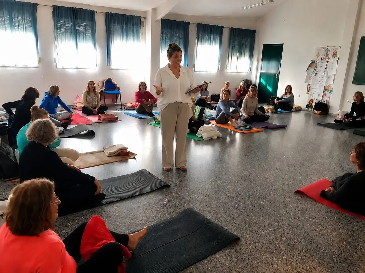 Personas sentadas en esterillas de yoga en una sala luminosa, con un instructor de pie en el centro.