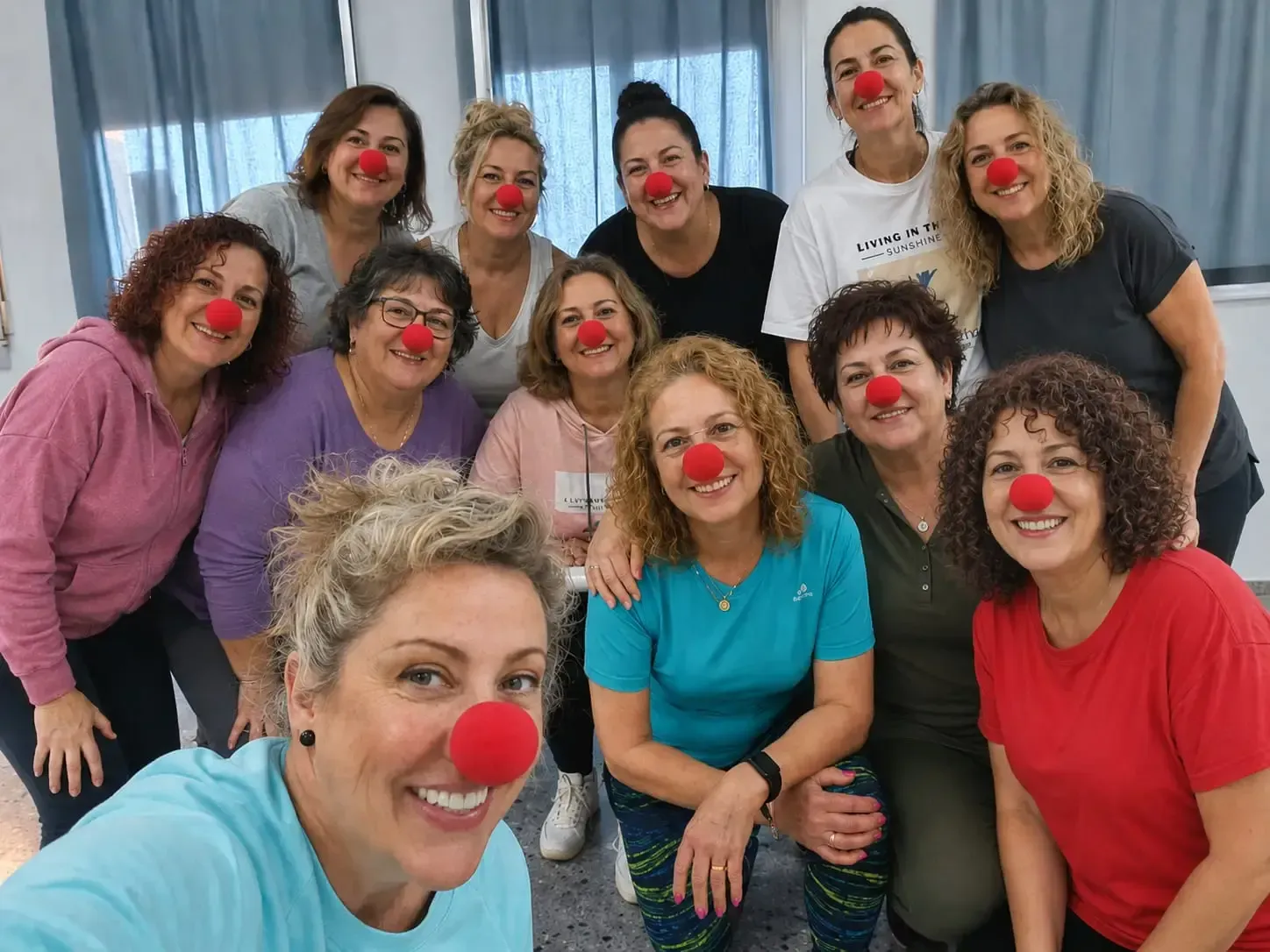 Nueve personas con narices rojas de payaso posan juntas en un interior, sonriendo a la cámara.