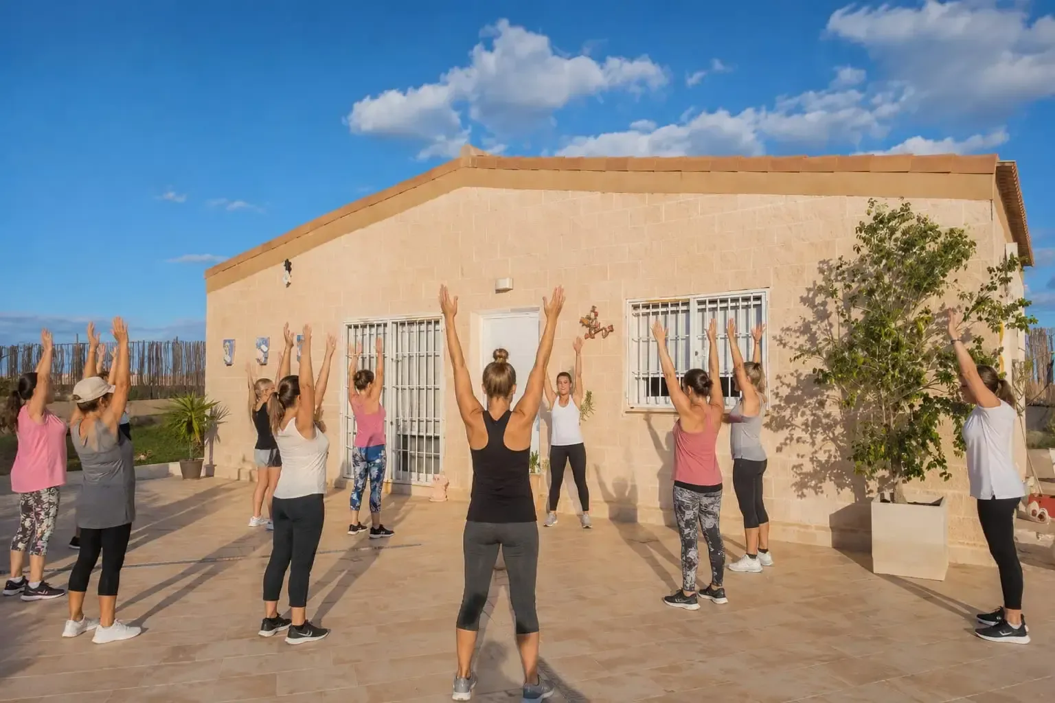Personas haciendo ejercicio al aire libre frente a un edificio de estuco color beige bajo un cielo azul