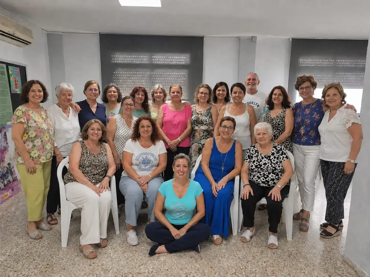 Grupo de personas posando juntas en una sala luminosa, sonriendo, unas sentadas y otras de pie en dos filas.