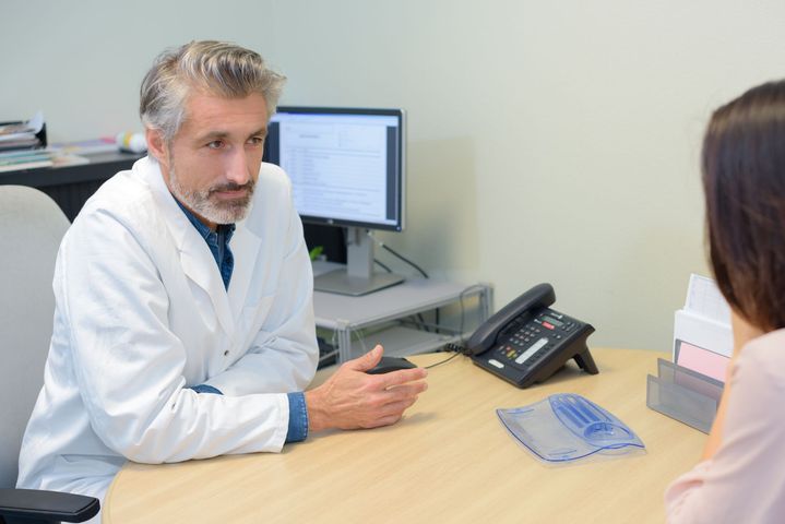 Un médecin consulte un patient à un bureau dans un cabinet médical, avec un ordinateur et un téléphone à proximité.