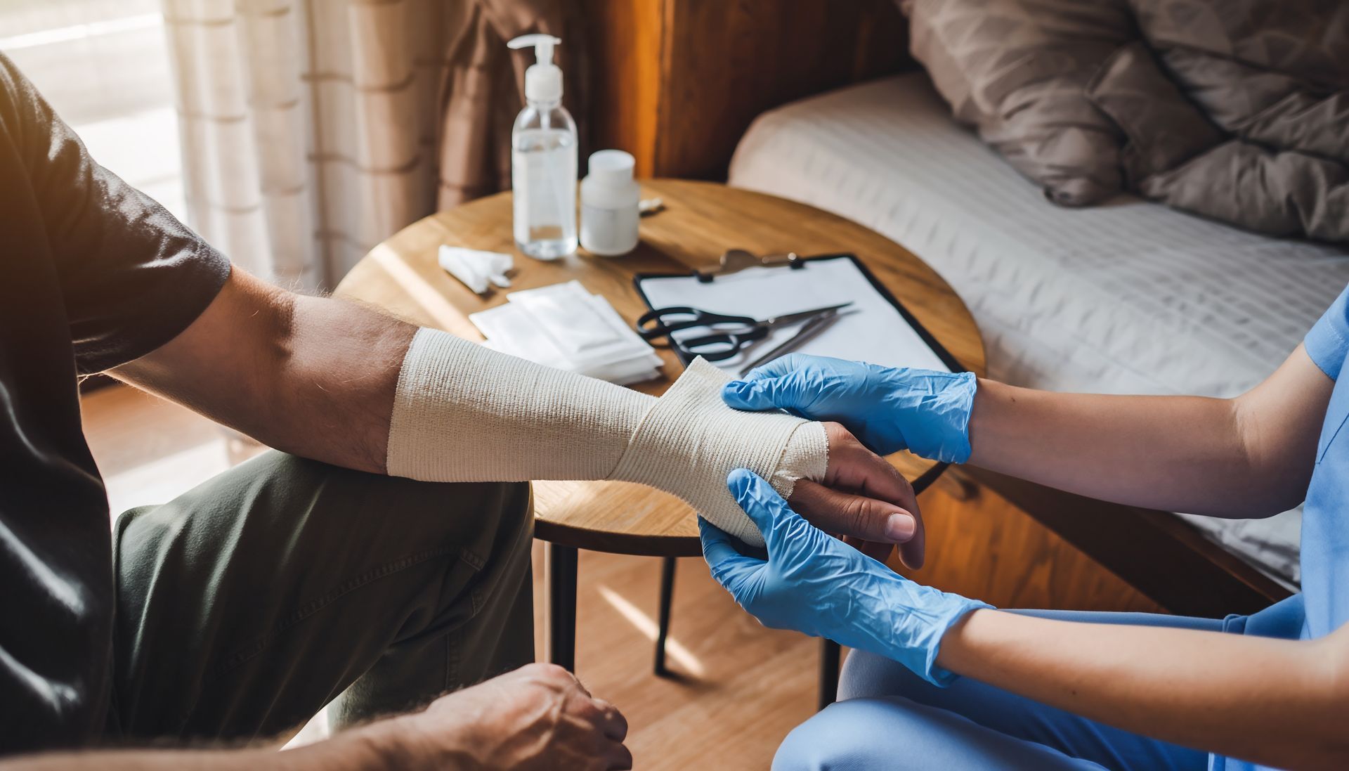 Un soignant ganté bande l'avant-bras d'un patient à domicile.