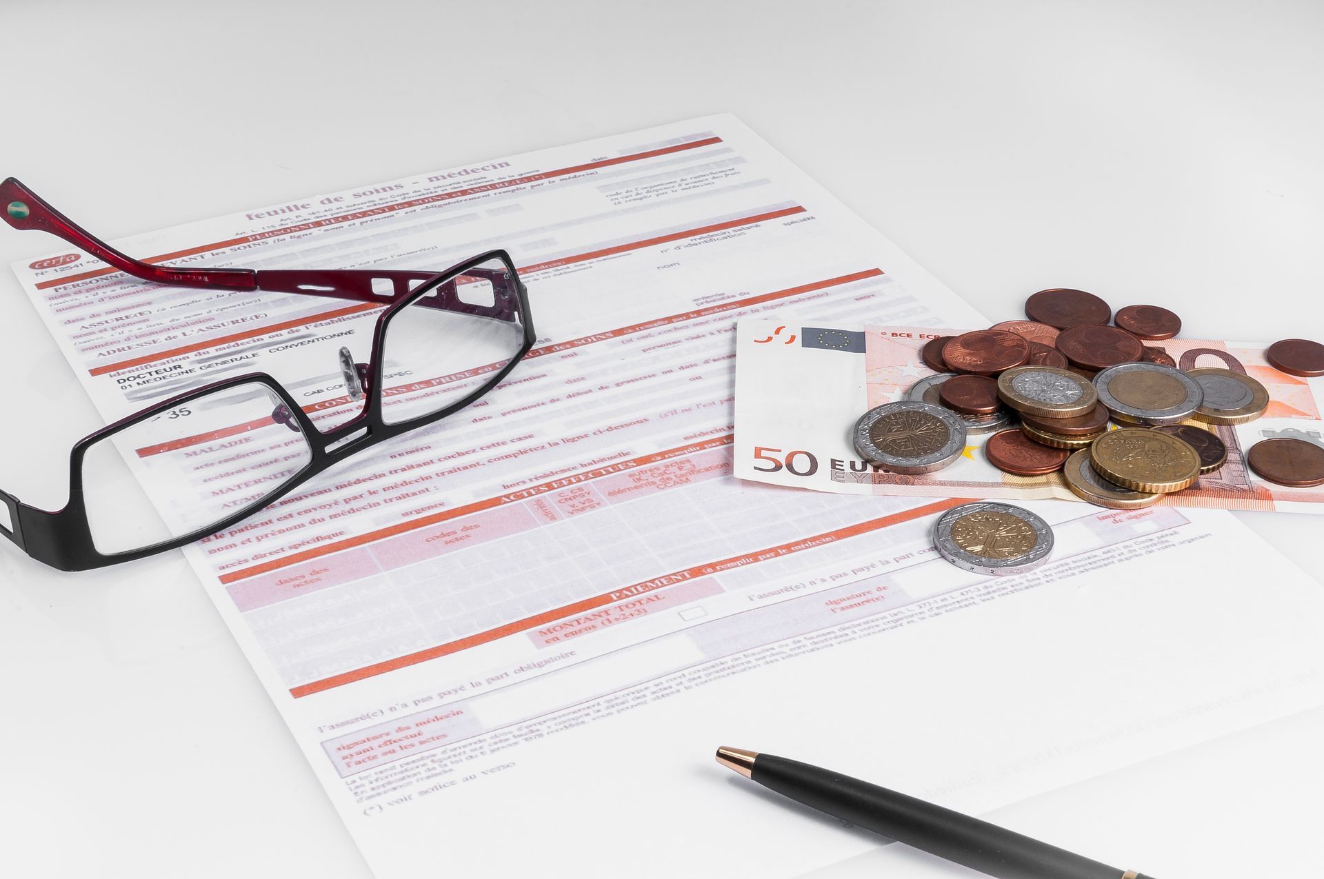 Lunettes, stylo et pièces de monnaie sur un document financier avec des billets en euros.