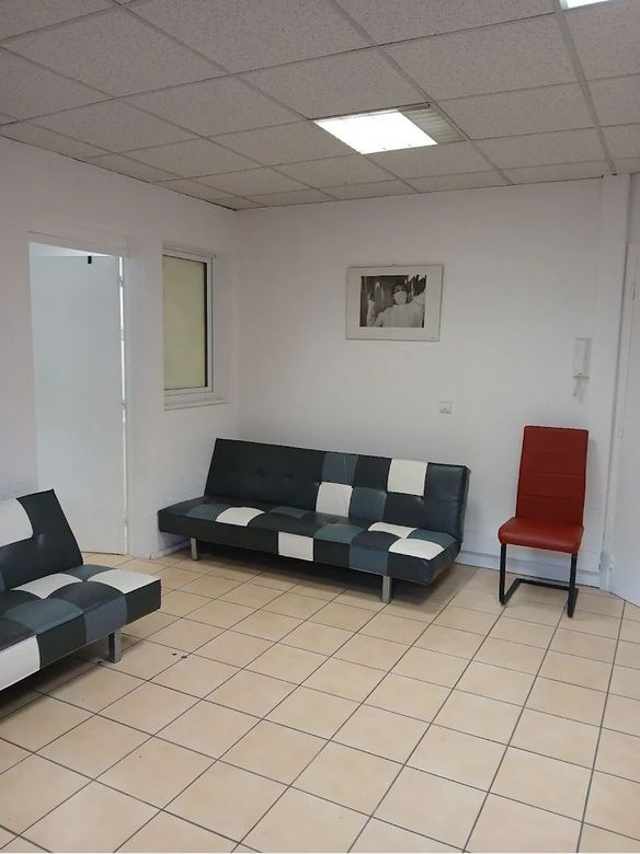 Salle d'attente vide avec canapés noirs et blancs, chaise rouge, sol carrelé et tableaux encadrés.