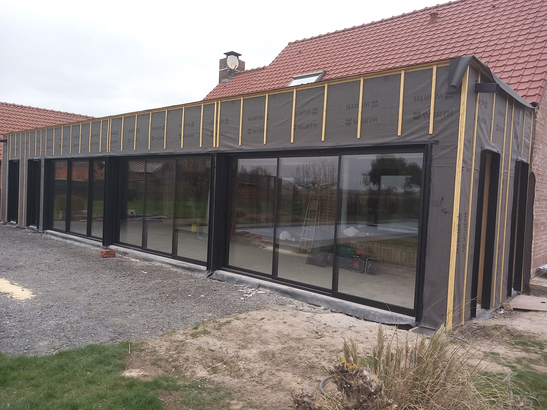Extérieur d'un bâtiment en construction, montrant des murs en briques avec des ouvertures de fenêtres