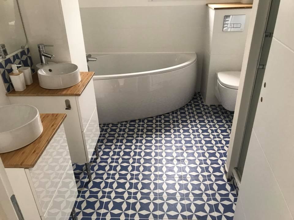 Salle de bains avec sol à motifs bleus, murs blancs, lavabos ronds et baignoire incurvée