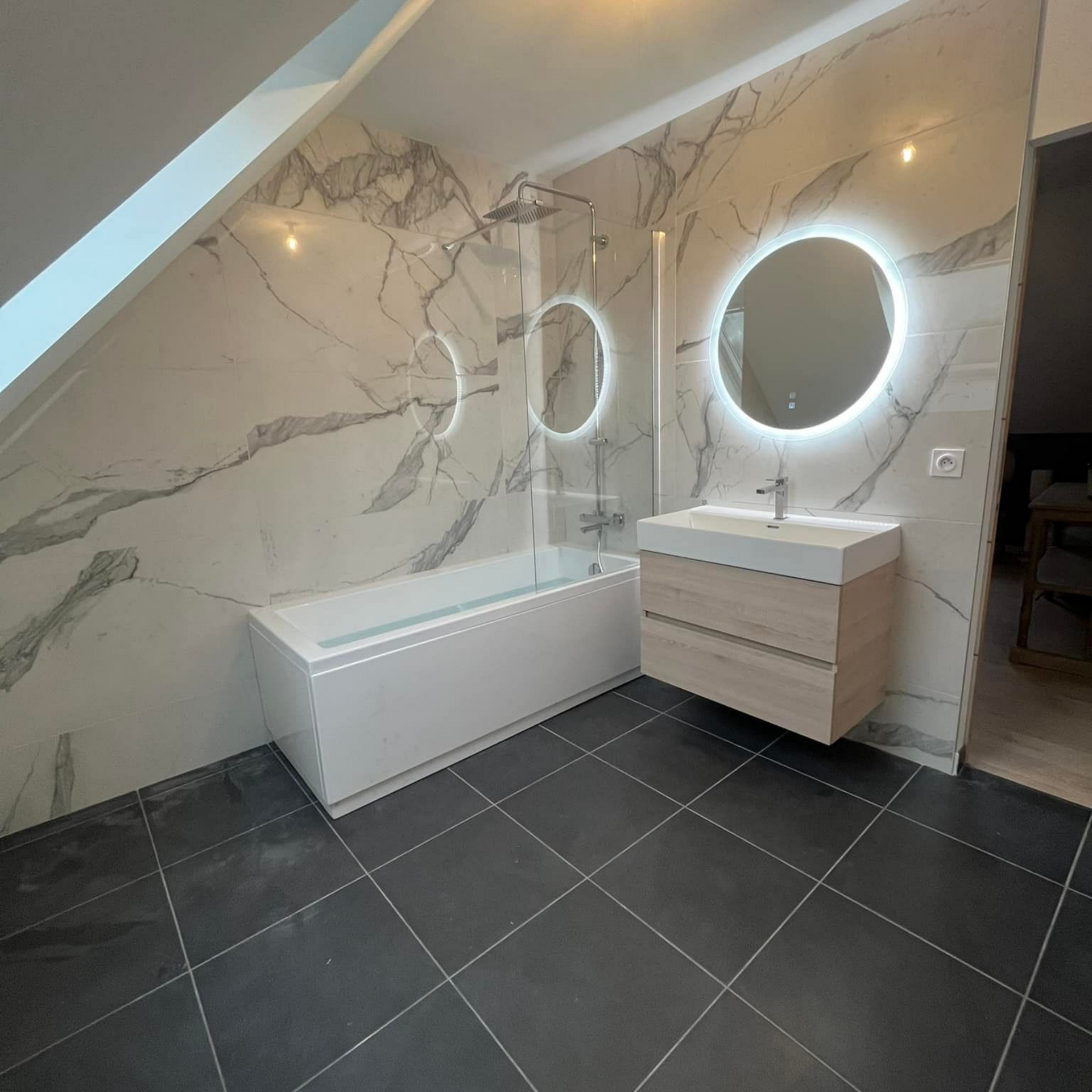 Salle de bains moderne avec mur en marbre, baignoire, vanité flottante et miroir rond rétroéclairé