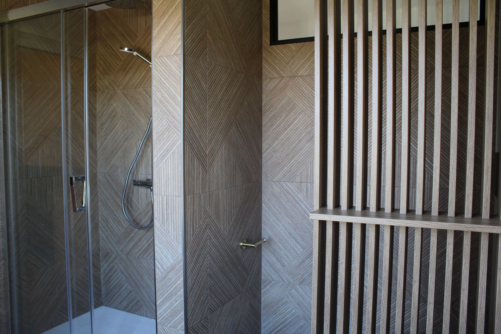 Salle de bains avec douche en verre, murs bruns texturés et séparateur en lattes de bois