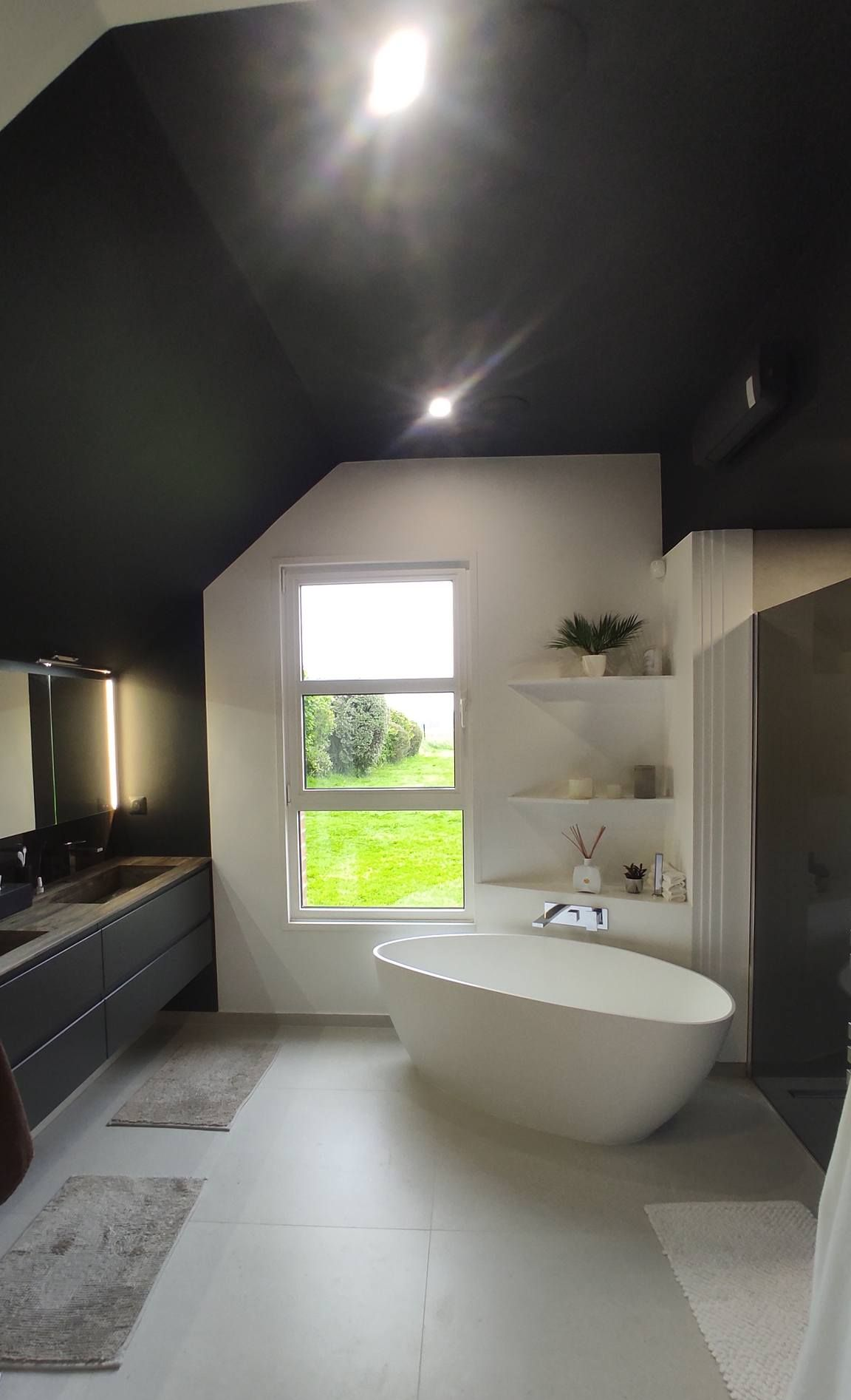 Salle de bains moderne avec baignoire, plafond noir et fenêtre donnant sur la verdure