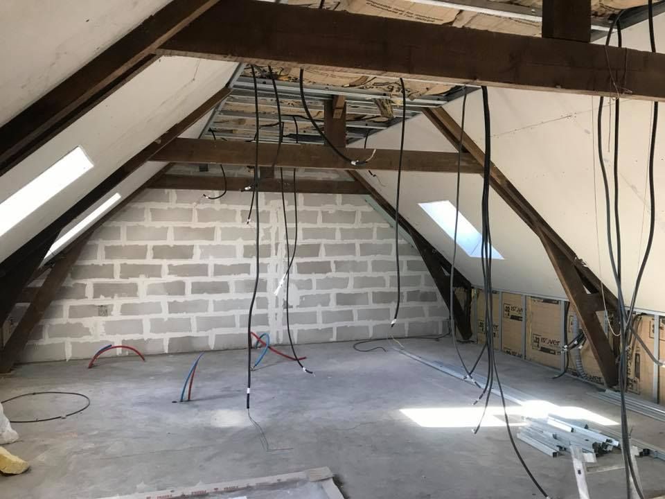 Grenier en construction avec câblage apparent, mur en parpaings, poutres en bois et plafond brut