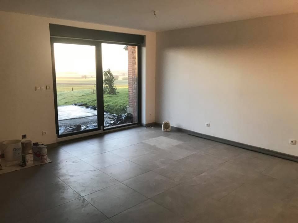 Pièce vide avec grande fenêtre, sol carrelé gris, murs blancs