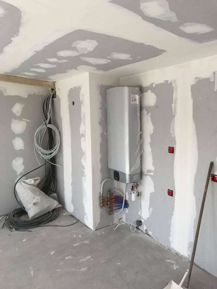 Chantier de construction intérieur avec cloisons sèches, plomberie et câblage électrique visibles.