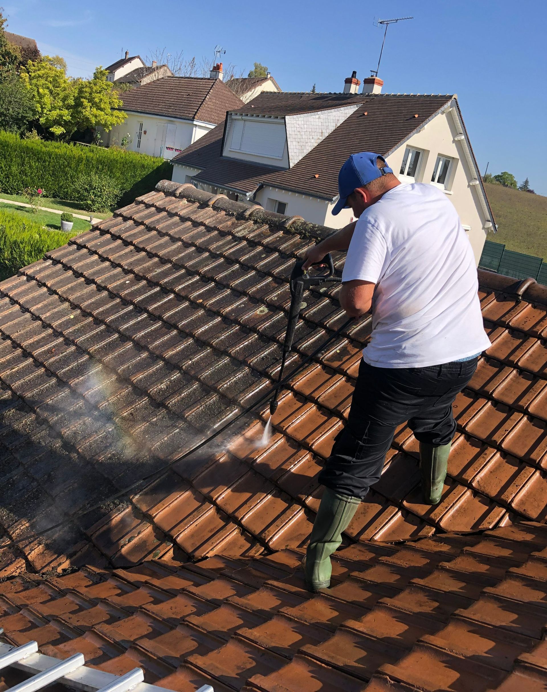 Un artisan en tee-shirt blanc en train de nettoyer une toiture au jet haute pression