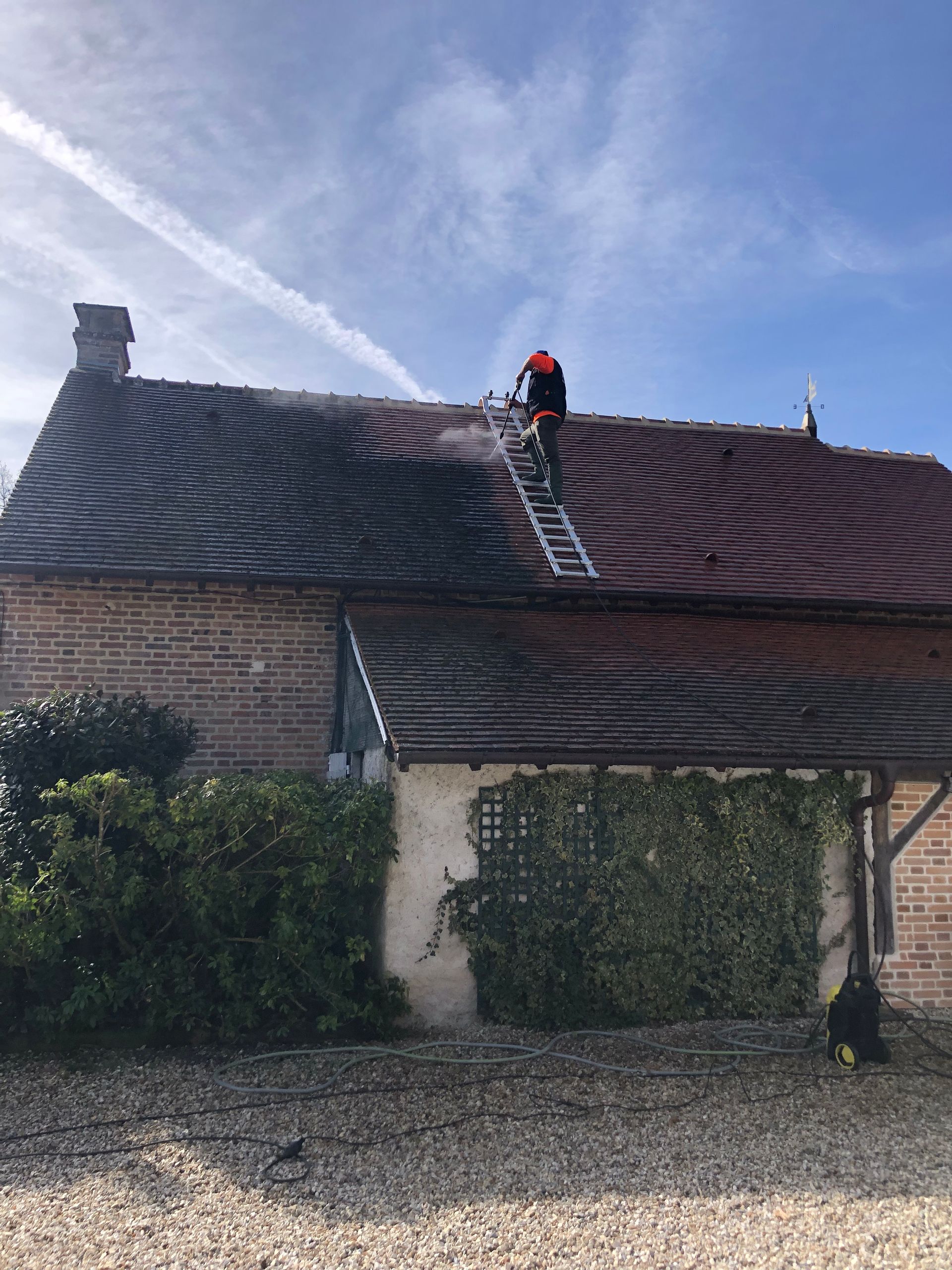 Un artisan sur une échelle en train de nettoyer les tuiles au jet haute pression