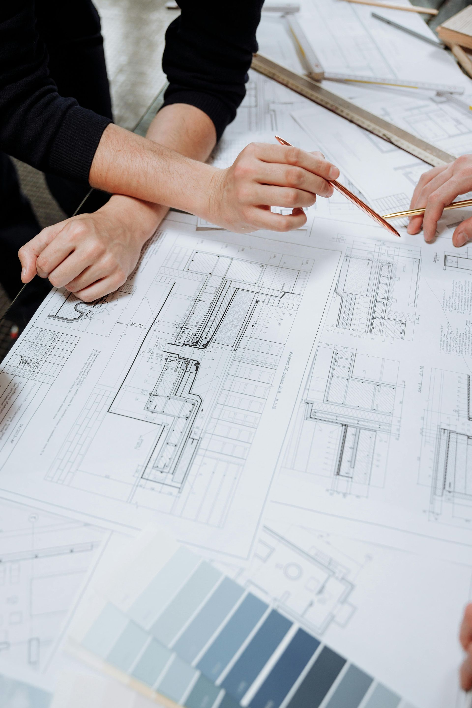 Des mains et des crayons examinant des plans d'architecte et des échantillons de couleurs sur un bureau
