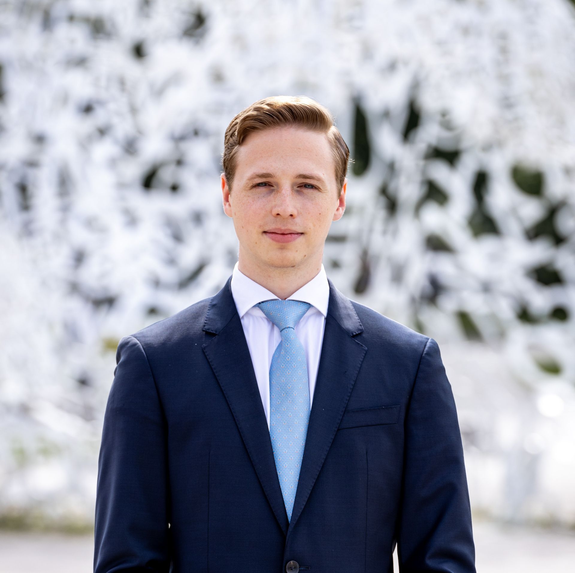 Ein Mann in Anzug und Krawatte steht vor einer weißen Wand.