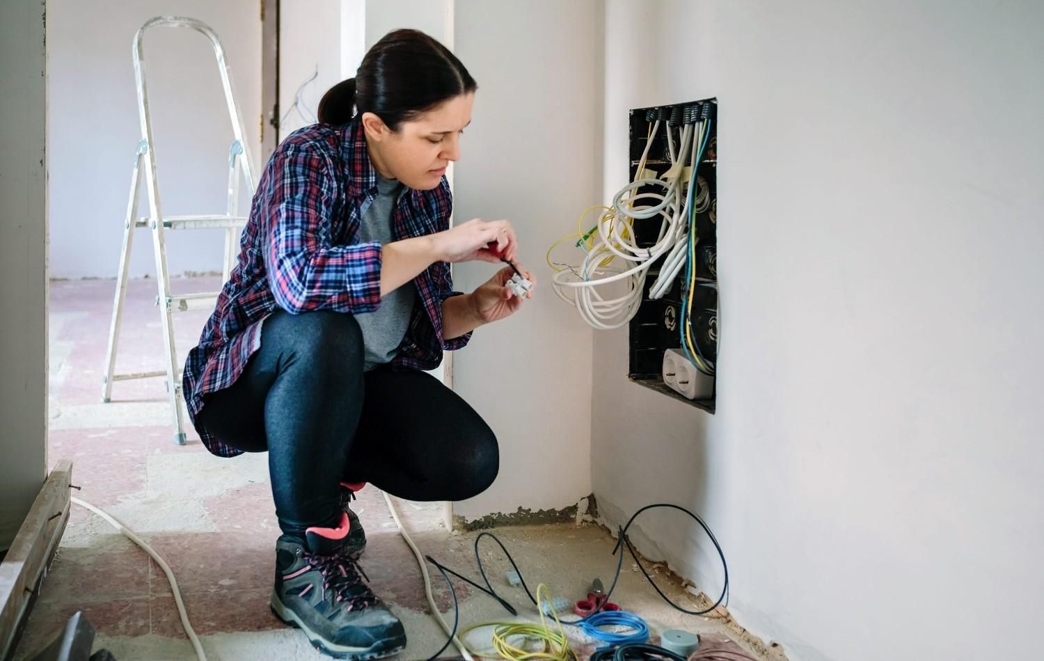 Electricista agachado junto a un panel de pared, organizando cables enredados durante un trabajo eléctrico.
