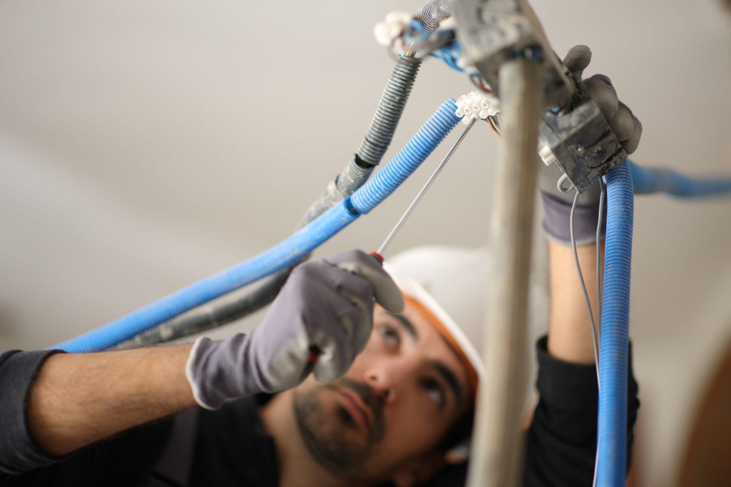 Técnico instalando cables azules con una llave inglesa, trabajando en el techo.