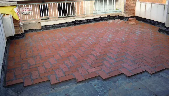 Terraza plana de ladrillo rojo en la azotea con barandilla y edificios circundantes en los bordes.
