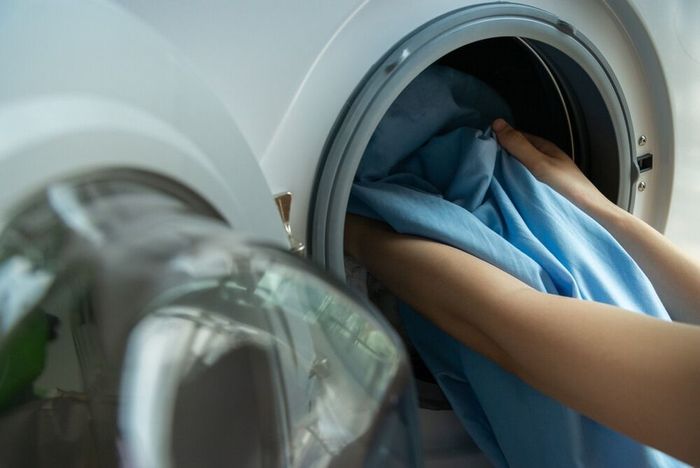 Una persona está poniendo una camisa azul en una lavadora.