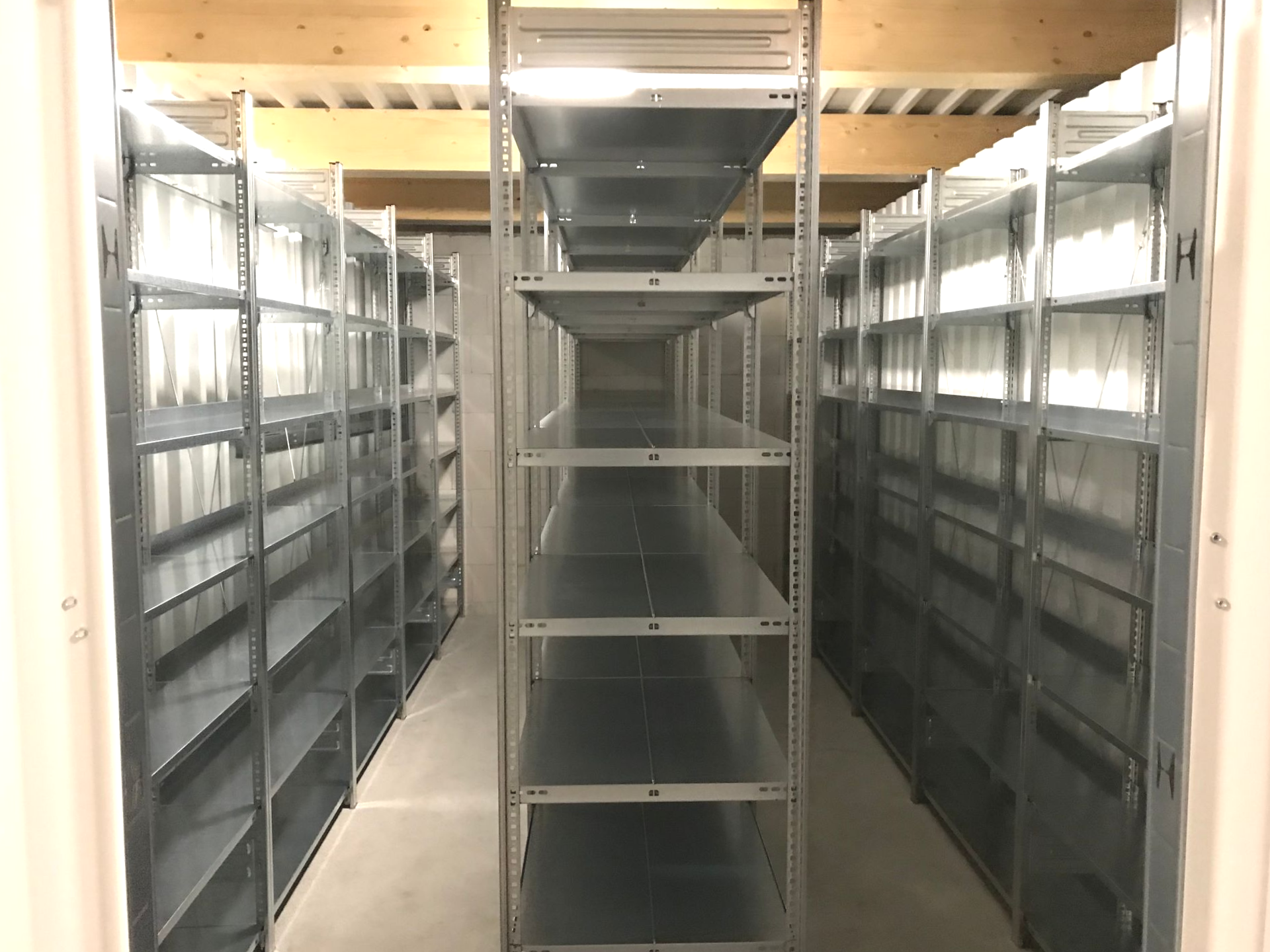 Metallregale in einem Lagerraum. Mehrere Regalreihen auf beiden Seiten mit einem Mittelgang.