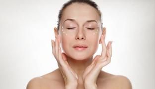 Una mujer se aplica crema en la cara con los ojos cerrados.