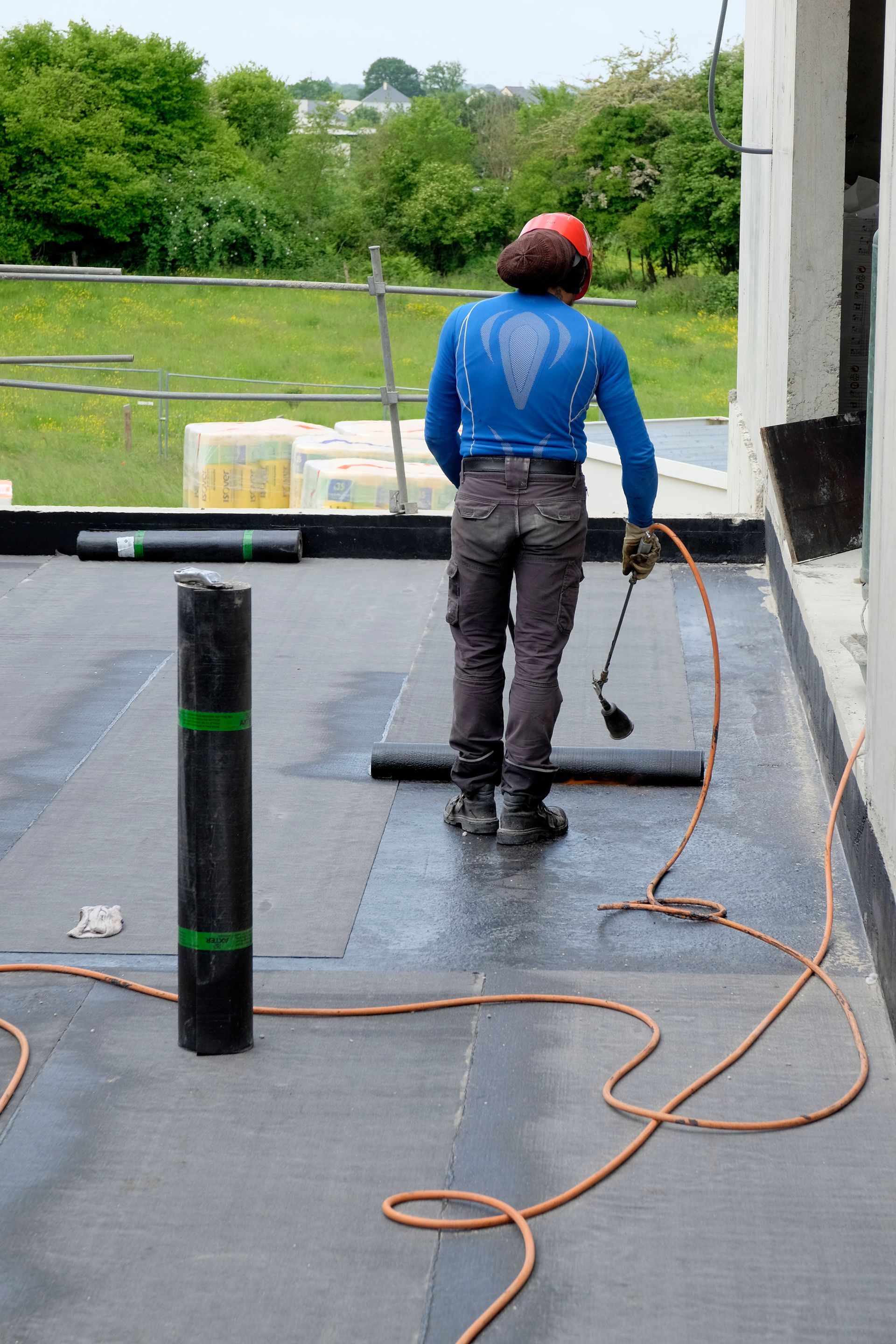 Un couvreur utilise un chalumeau pour appliquer un matériau de couverture sur un toit plat.