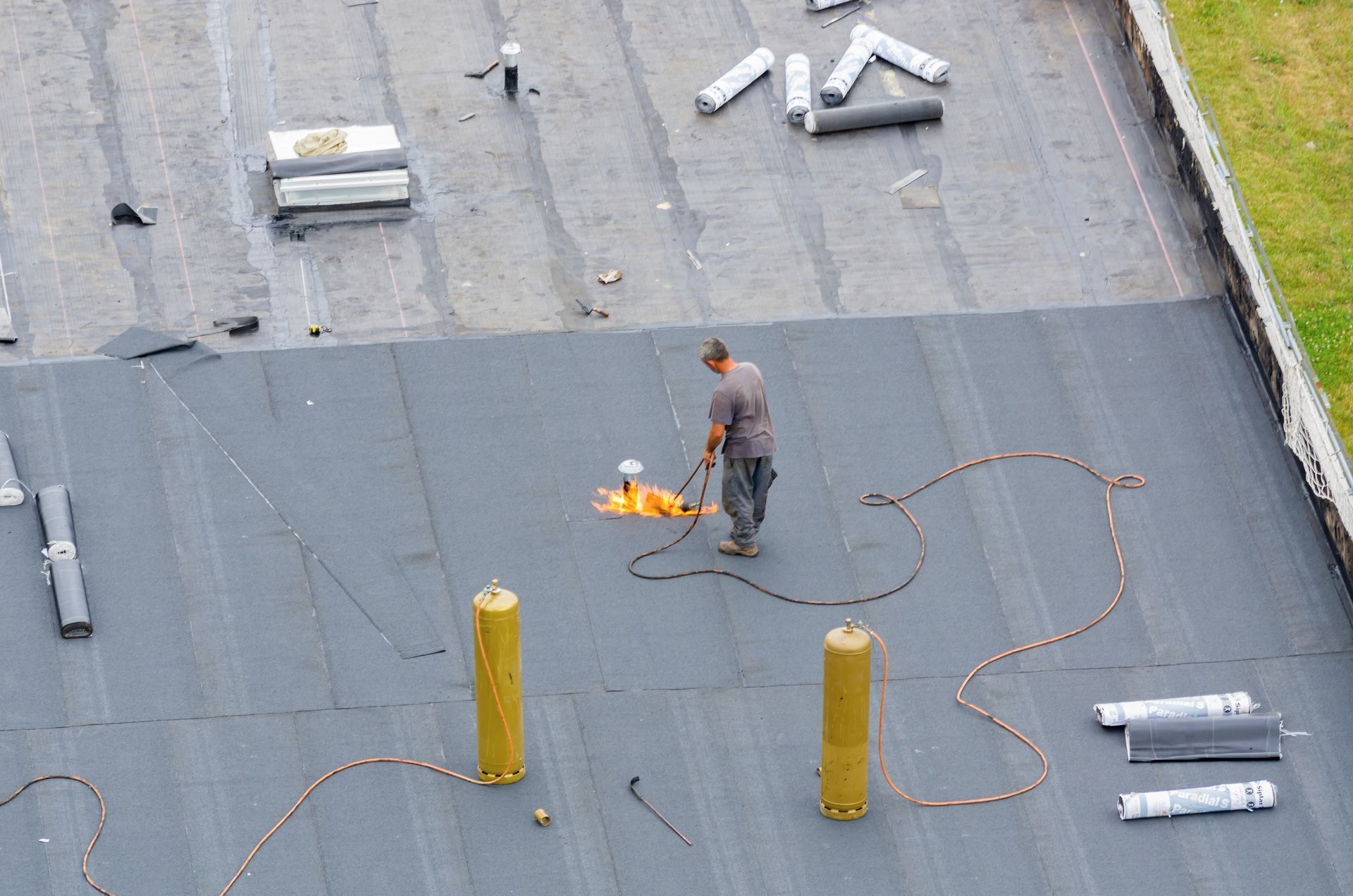 Couvreur sur un toit plat gris foncé, utilisant son matériel.