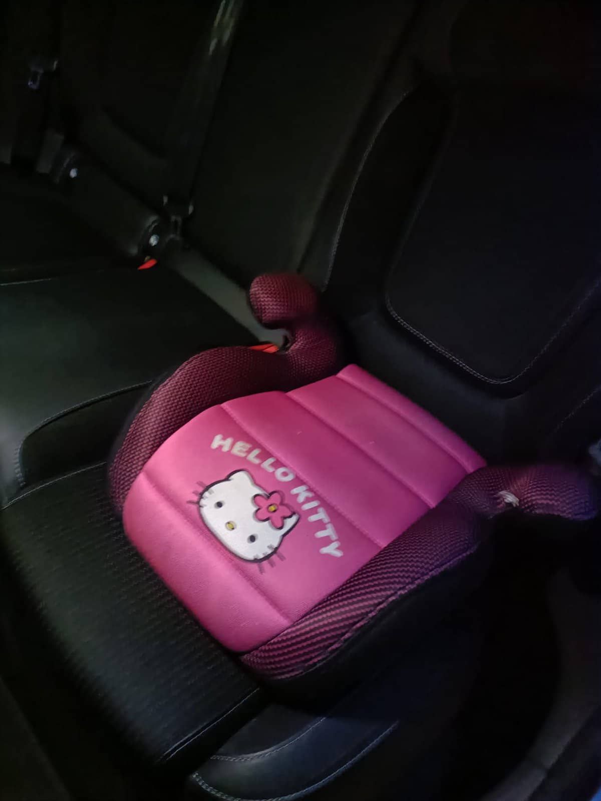 Asiento elevador para automóvil de Hello Kitty de color rosa sobre un asiento de automóvil de color negro.
