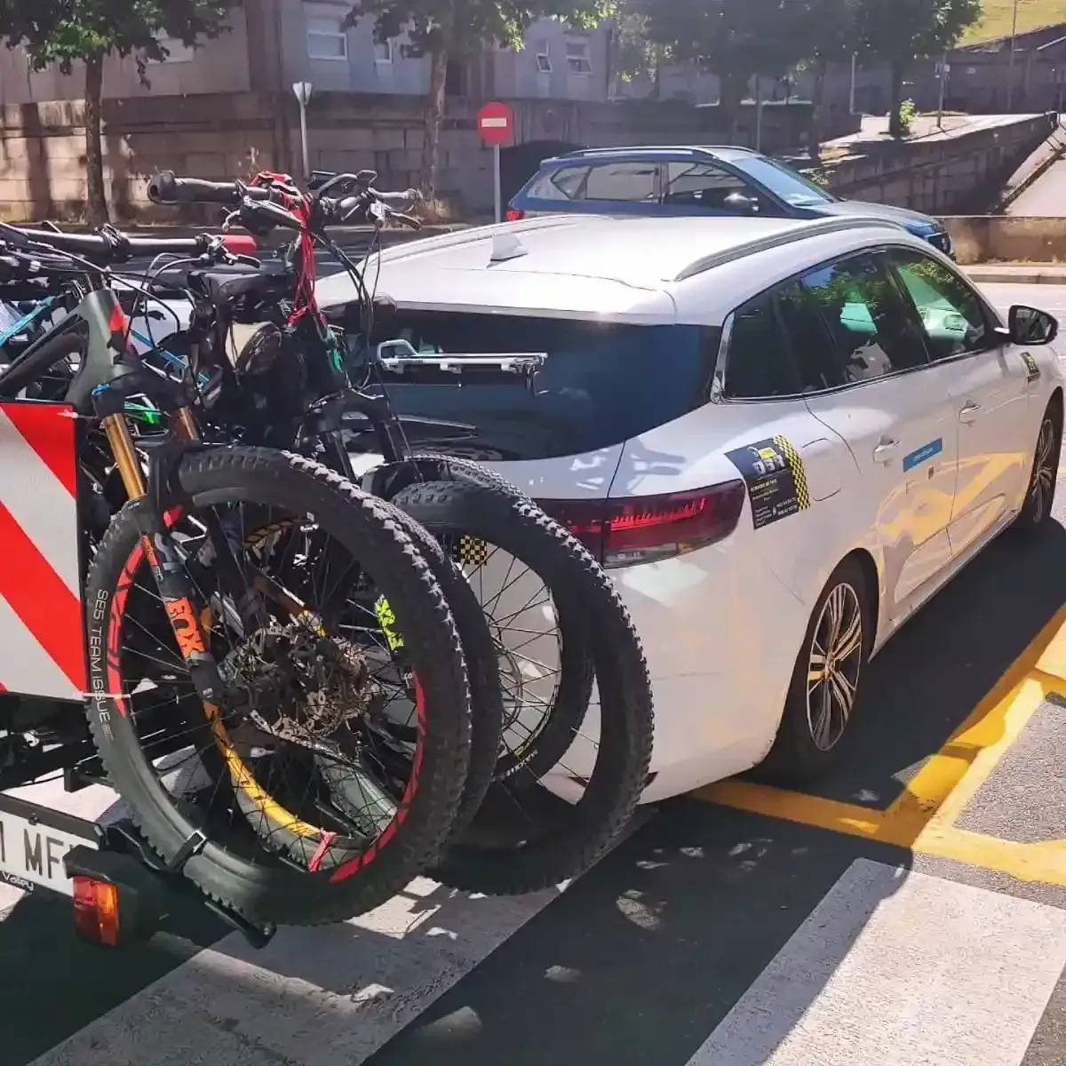 Coche blanco con dos bicicletas de montaña montadas en un portabicicletas; aparcado al aire libre.