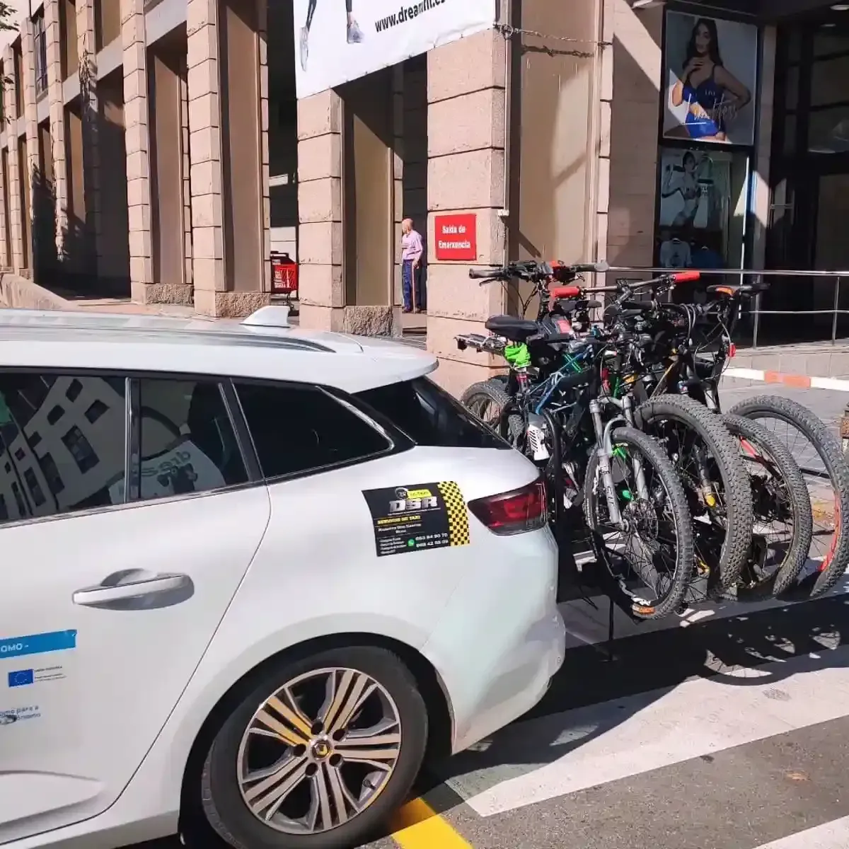 Automóvil blanco con bicicletas en un soporte estacionado cerca de un edificio.