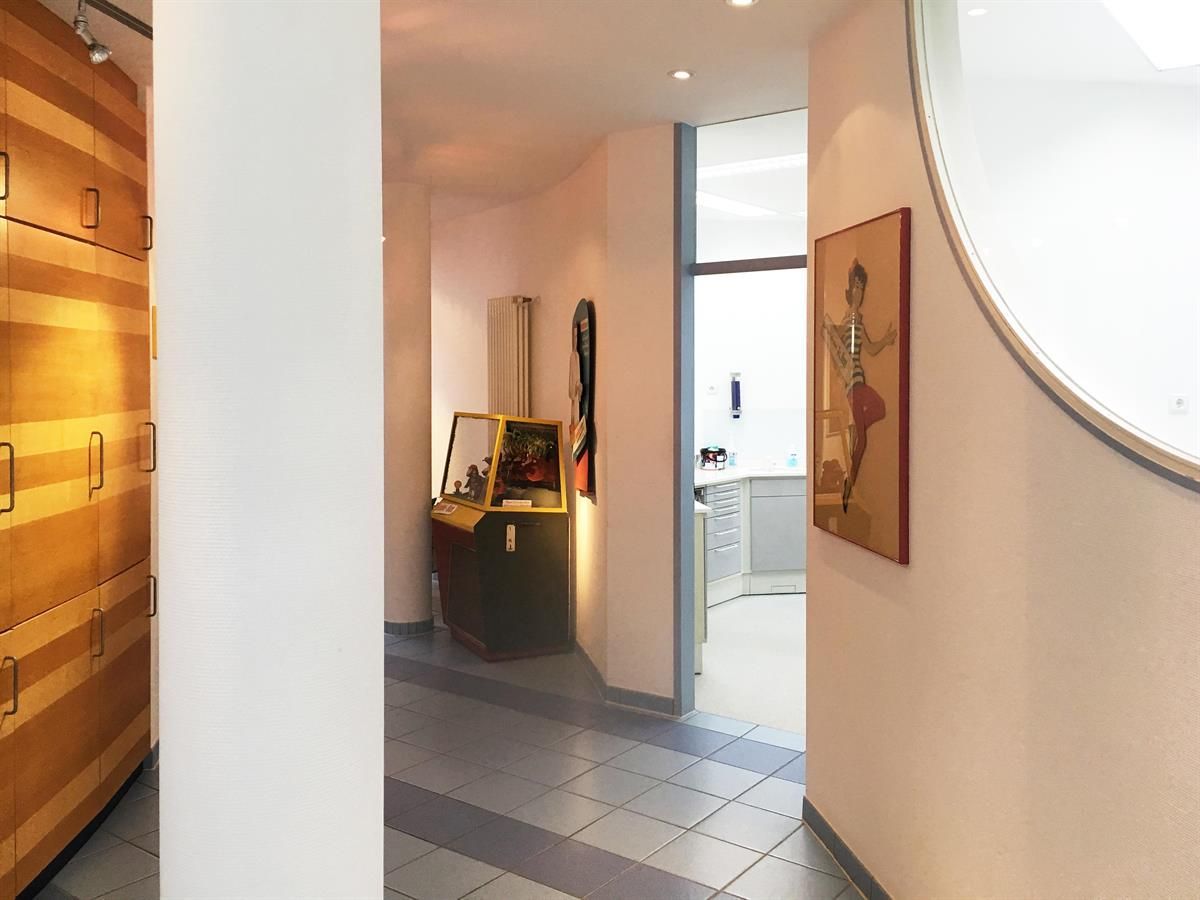 Flur mit blauem Fliesenboden, weißen Wänden und einem Holzschrank auf der linken Seite. An der rechten Wand hängt ein Gemälde.