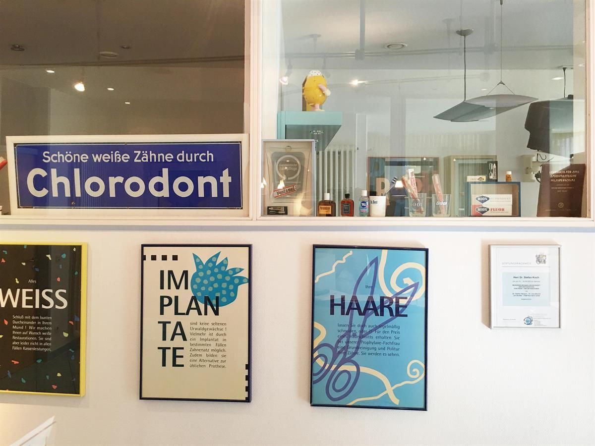 Das Interieur einer Zahnarztpraxis mit gerahmten Postern und einem Fenster mit einem Schild für „Chlorodont“.