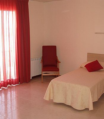 Un dormitorio con una cama, una silla y cortinas rojas.