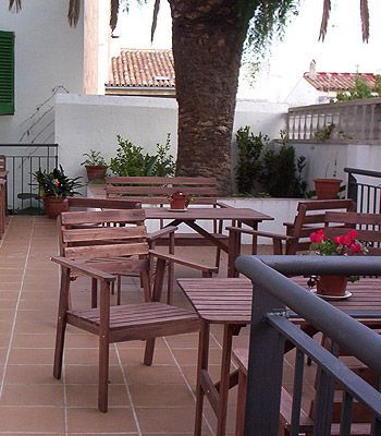 Sillas y mesas de madera en un patio con una palmera al fondo