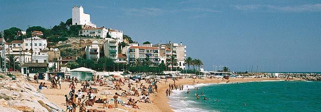 Una playa con mucha gente y edificios al fondo.