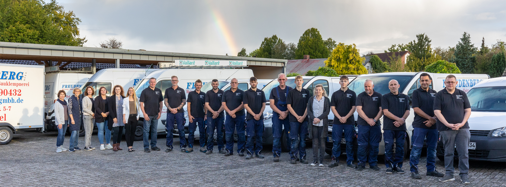 Eine Gruppe von Menschen posiert vor einer Reihe von Lieferwagen für ein Foto.