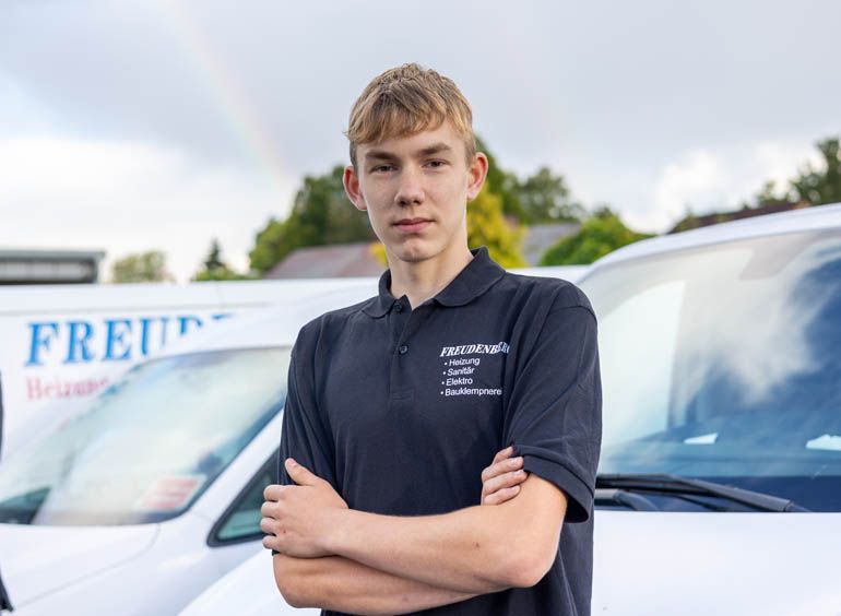 Ein junger Mann steht mit verschränkten Armen vor einem Lieferwagen.