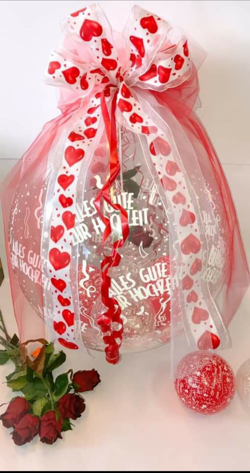 Ein Luftballon mit einer Schleife und Herzen darauf liegt neben Rosen auf einem Tisch.