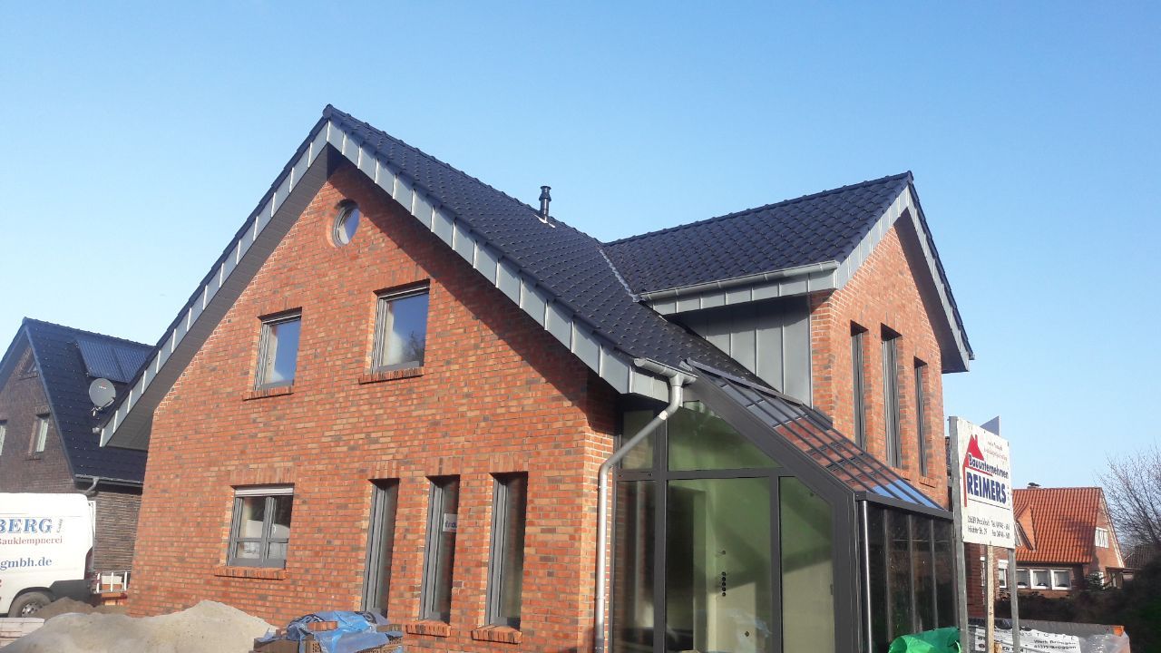Ein Backsteinhaus mit schwarzem Dach und einem Gewächshaus