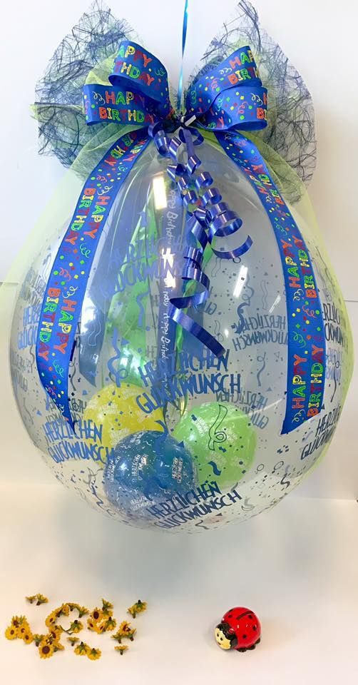 Ein durchsichtiger Ballon gefüllt mit Luftballons und einer blauen Schleife.